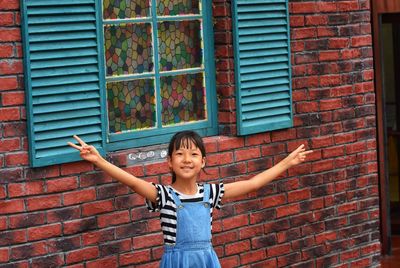 Portrait of happy girl standing against brick wall