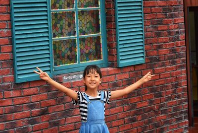 Portrait of happy girl standing against brick wall