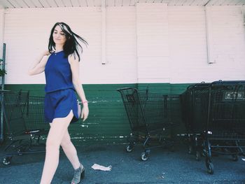 Fashionable woman wearing blue dress walking against wall in city