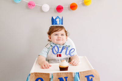 Cute smiling caucasian baby boy in blue crown celebrating his first birthday at home. 