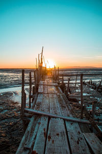 Wooden posts on beach against sky during sunset