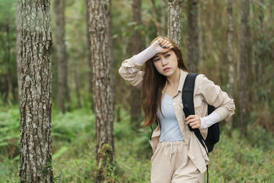 Young woman standing against tree trunk in forest