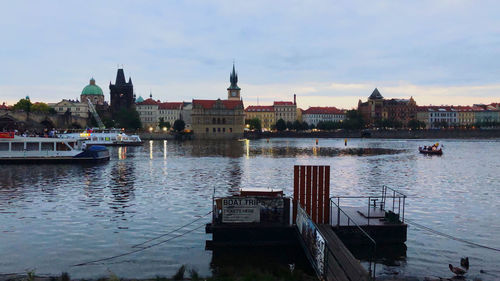 Boats moored in river by buildings against sky