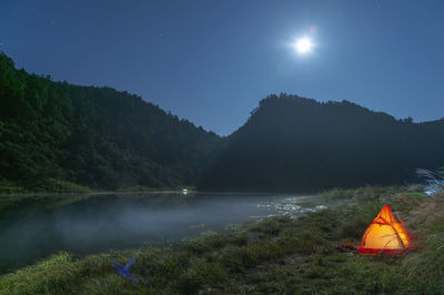 Tent on mountain by lake against sky at night
