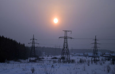 Electricity pylon on snow field against sky during sunset