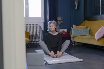 Senior woman doing yoga through online tutorial on laptop at home