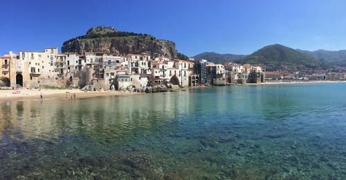 Scenic view of town by sea against clear blue sky