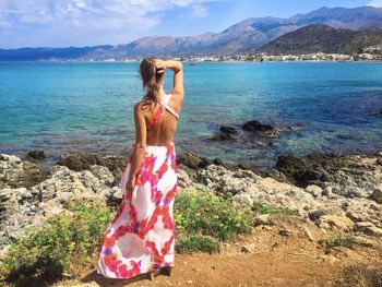 Rear view of woman with long dress standing near an exotic beach