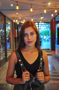 Portrait of young woman standing in illuminated room