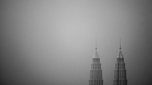 Petronas towers against clear sky during foggy weather at night