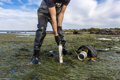 Low section of man on field by sea against sky