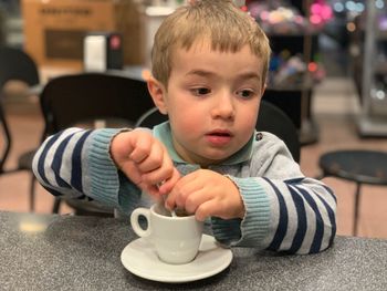 Close-up of cute boy looking away while sitting with coffee cup on table at cafe