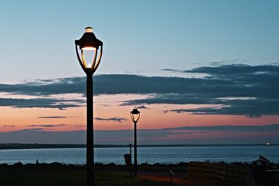 Street light by sea against sky during sunset