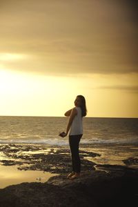 Full length of woman standing on beach against sky during sunset