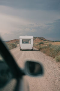 Through car side mirror view of straight roadway with caravan against mountain rural landscape