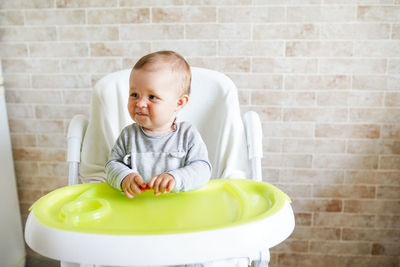 Cute baby girl sitting on high chair against wall