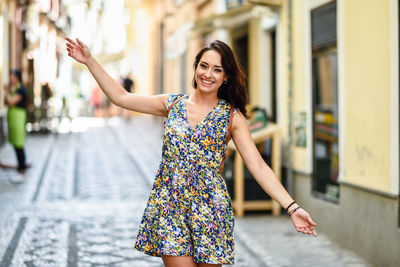 Portrait of happy woman standing with arms outstretched at street