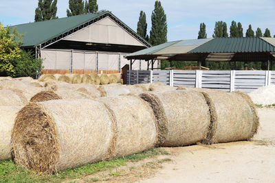 Hay bales on field by houses against sky