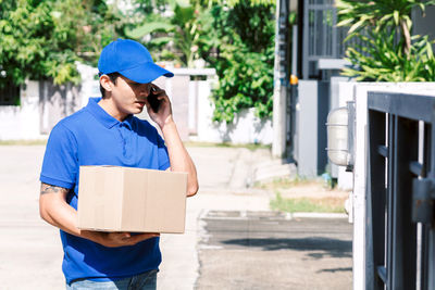 Salesman carrying box while talking on phone by gate