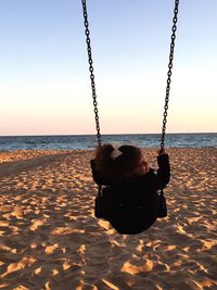 Rear view of girl playing on swing at beach