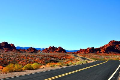 Country road leading towards mountains against blue sky