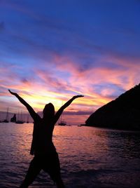 Silhouette children playing in sea against sky during sunset