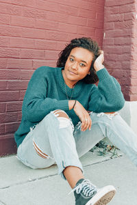 Portrait of a young woman sitting against brick wall