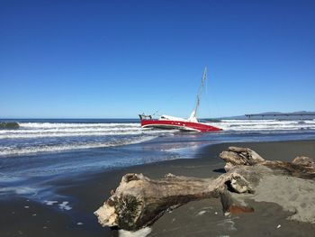 Sailboat on sea shore against clear blue sky