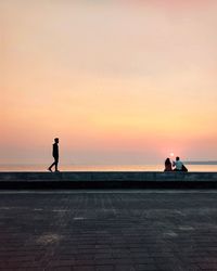 Silhouette people on shore against orange sky