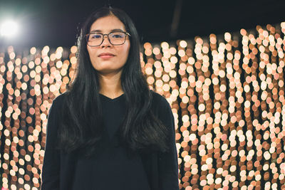 Portrait of young woman standing against illuminated lights