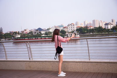 Full length of woman standing on railing against cityscape