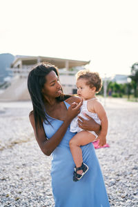 Mother and daughter standing on beach against sky