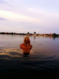 Rear view of woman swimming in lake against sky during sunset