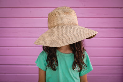 Portrait of little girl hiding her face under big straw hat