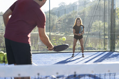 Young man playing paddle tennis with woman on sunny day