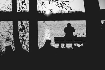 Rear view of silhouette woman standing by water against sky