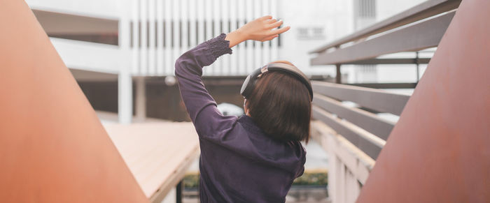 Rear view of woman listening music against building