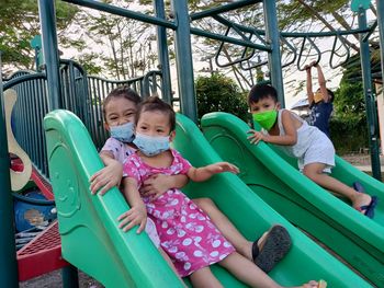 Portrait of siblings sitting on slide at playground