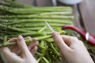 Cropped hand of woman cutting asparagus on table at home