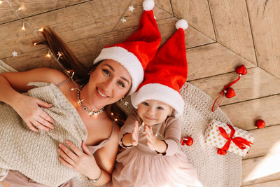 Happy family, cute mom and baby little daughter in  santa hats having fun on the floor at christmas