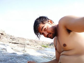 Close-up of shirtless young woman at beach against clear sky