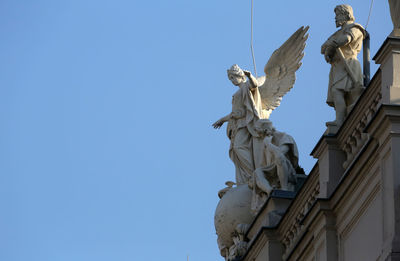 Low angle view of angel statue on roof against blue sky