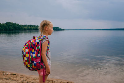 Girl wearing backpack while standing at beach against sky