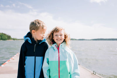 Brother and sister stood on a pier at the beach smiling