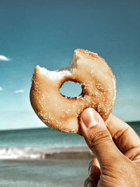 Cropped hand of woman holding donut at beach