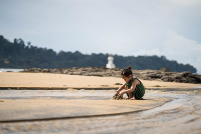 Side view of girl sitting on land at beach against sky