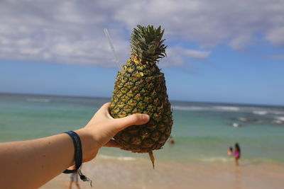 Close-up of hand holding fruit on beach against sky