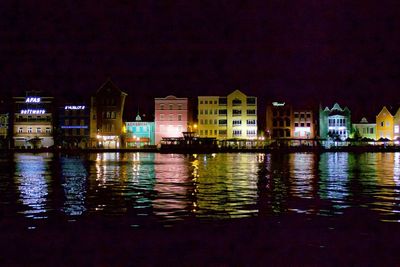 Illuminated buildings by river against sky at night