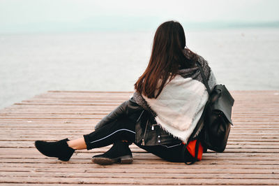 Side view of woman sitting on pier over lake