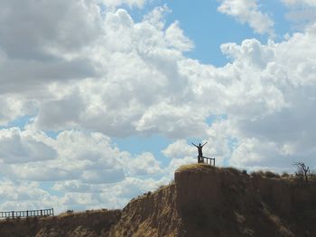 Low angle view of person standing on landscape against cloudy sky